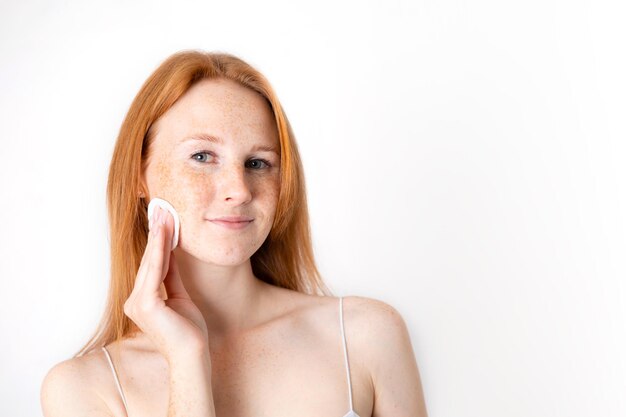 Una joven y hermosa mujer pelirroja con pecas cuida la piel de la cara Selfcare Maquillaje natural Fondo blanco Espacio para texto