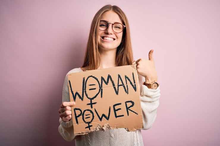 Foto joven hermosa mujer pelirroja pidiendo derechos de las mujeres sosteniendo una pancarta sobre fondo rosa feliz con una gran sonrisa haciendo bien firmar el pulgar hacia arriba con los dedos excelente señal