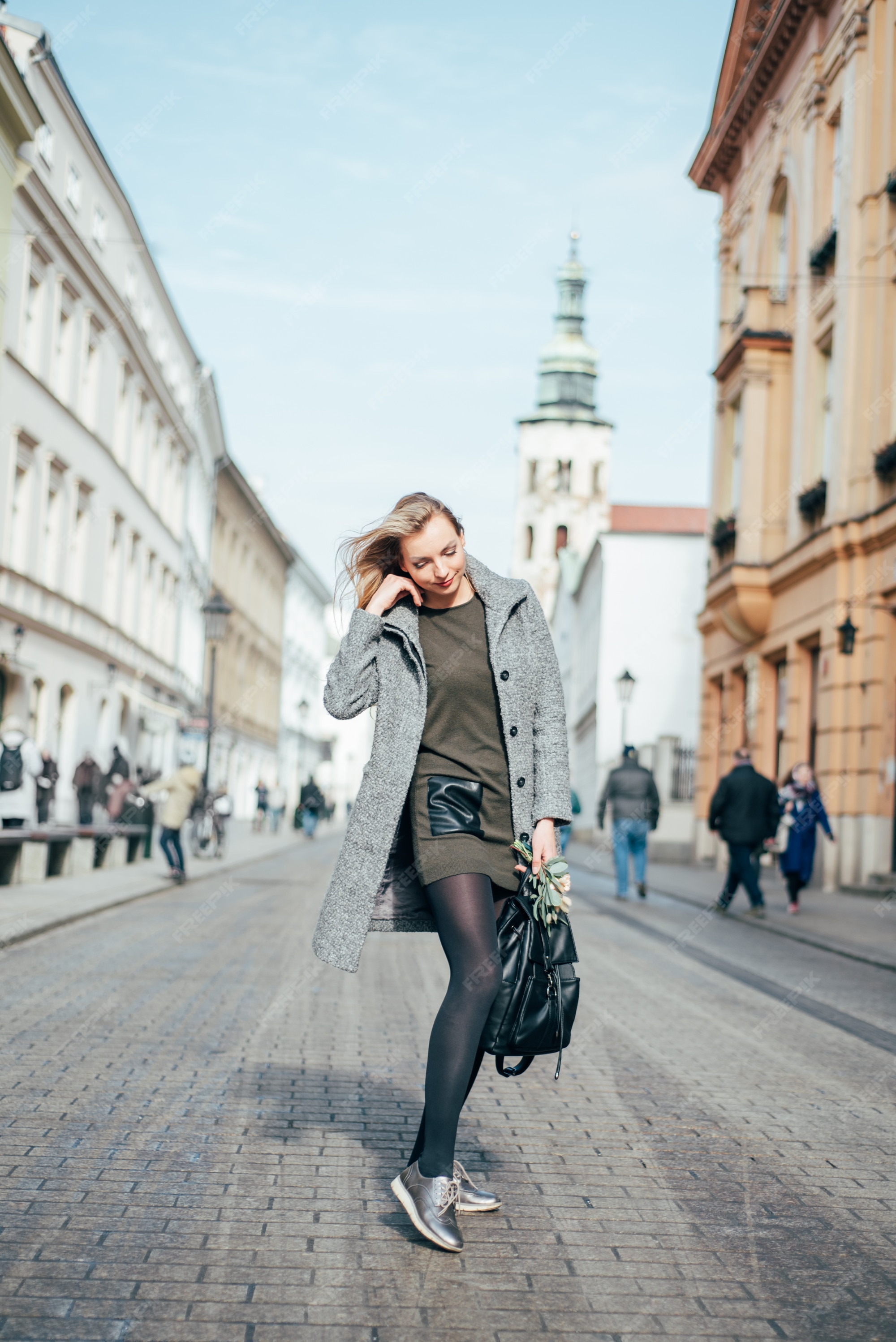 Joven hermosa mujer rubia en abrigo gris, vestido corto verde y medias negras caminando por las calles de la ciudad. | Foto Premium