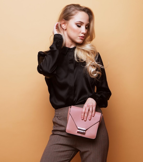 Joven hermosa mujer rubia con una blusa marrón y pantalones sostiene un bolso rosa