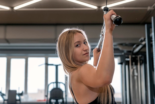 Joven hermosa mujer rubia entrena en el gimnasio Ejercicio desplegable Entrenamiento muscular de la espalda