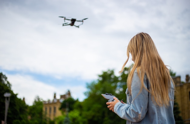 Joven hermosa mujer rubia pilotando un dron sosteniendo un control remoto en la mano