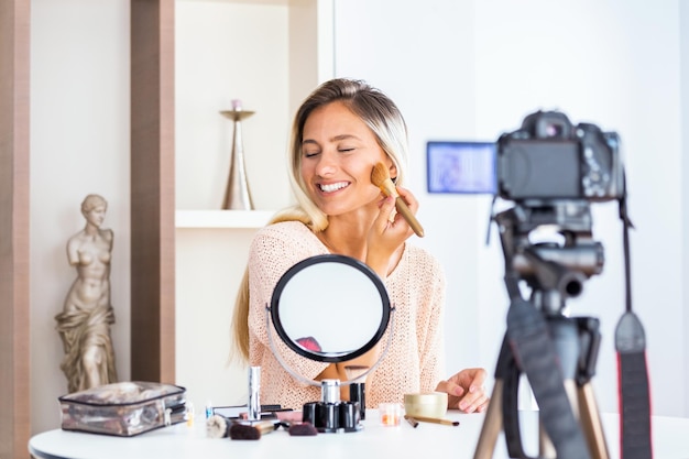 Joven hermosa mujer rubia profesional de belleza vlogger o blogger grabación de tutorial de maquillaje para compartir en las redes sociales