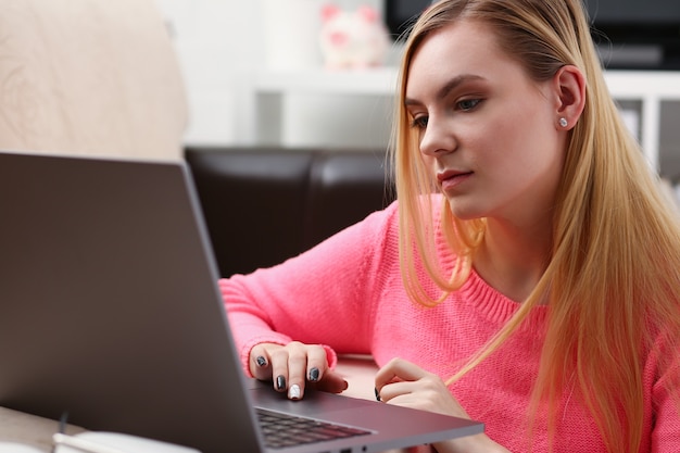 Joven hermosa mujer rubia sentada en el trabajo de la sala de estar en concepto de fines de semana agradables portátil