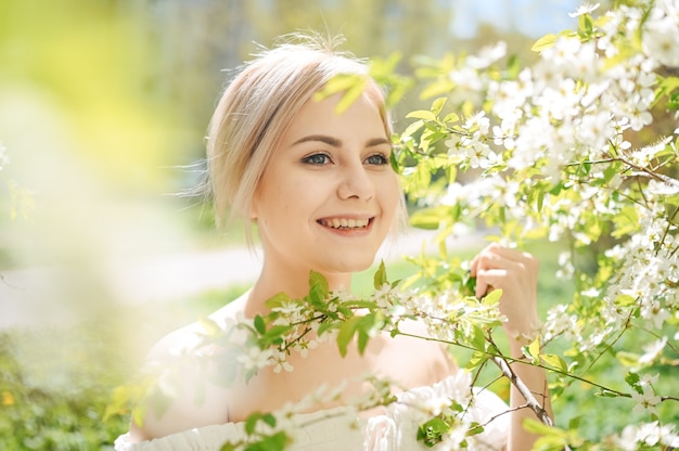 Joven hermosa mujer rubia sonriente feliz posando en el floreciente jardín de primavera con flores blancas