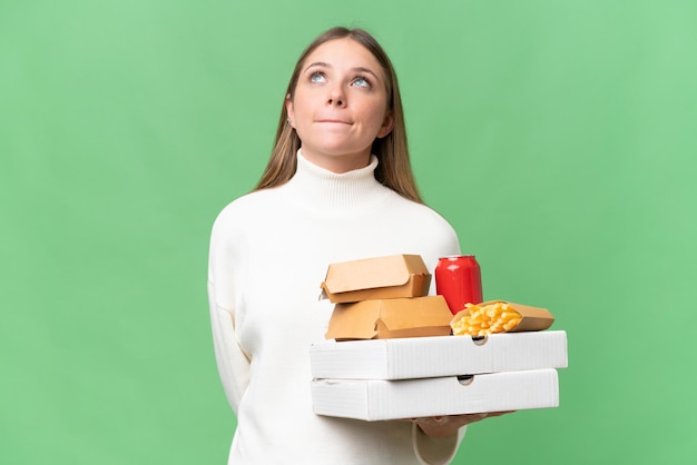 Joven hermosa mujer rubia sosteniendo comida para llevar sobre un fondo aislado y mirando hacia arriba