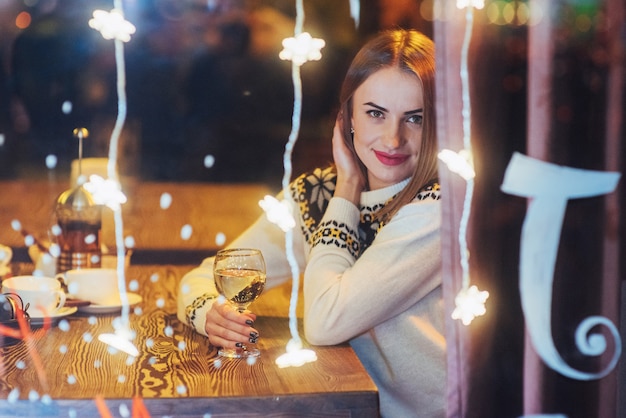 Joven hermosa mujer sentada en la cafetería, bebiendo vino. Navidad, año nuevo, día de San Valentín, vacaciones de invierno