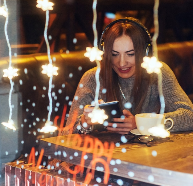 Foto joven hermosa mujer sentada en la cafetería, tomando café. modelo escuchando música.