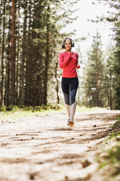 Joven hermosa mujer sonriente escuchando música y trotando en la naturaleza.