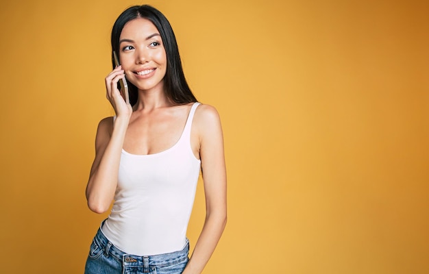 Joven hermosa mujer sonriente está hablando por teléfono con alguien aislado de fondo amarillo