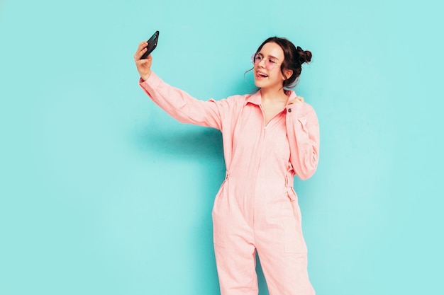 Joven hermosa mujer sonriente en un mono rosa de verano de moda Sexy mujer despreocupada posando junto a la pared azul en el estudio con dos cuernos Modelo positivo divirtiéndose y volviéndose loco Alegre y feliz