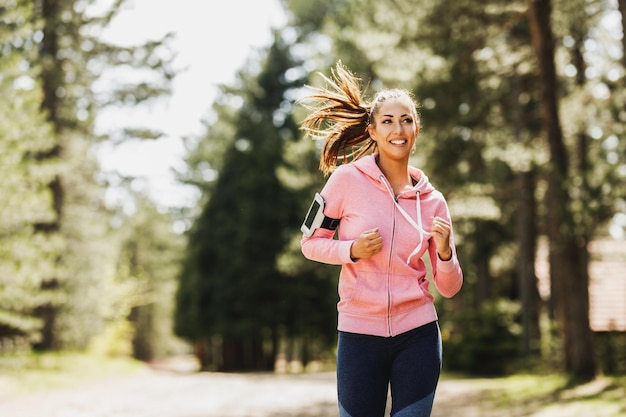 Joven hermosa mujer sonriente trotando por un sendero soleado en el bosque.