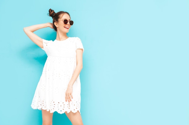 Joven hermosa mujer sonriente en vestido de verano de moda Mujer sexy despreocupada con peinado de dos cuernos posando junto a la pared azul en el estudio Modelo positivo divirtiéndose