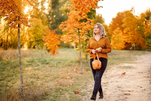 Joven hermosa mujer de talla grande con una camisa naranja y jeans camina en un parque de otoño