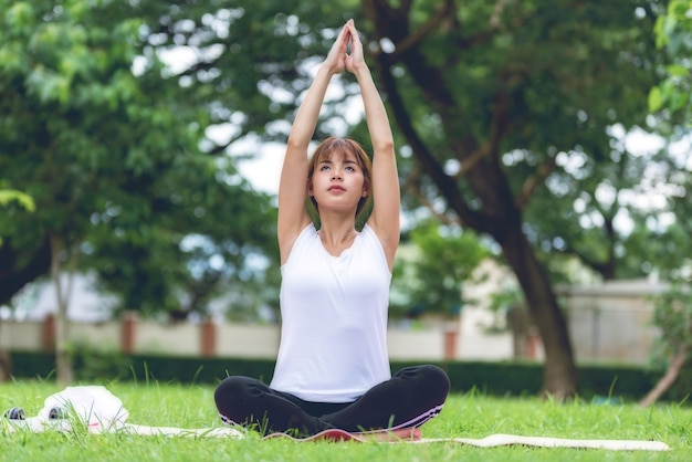 Joven hermosa mujer de yoga en el césped de verano con auriculares escuchando música y relajante