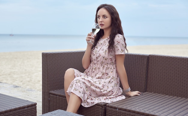 Joven hermosa niña brillante en un vestido de verano sentado en la playa