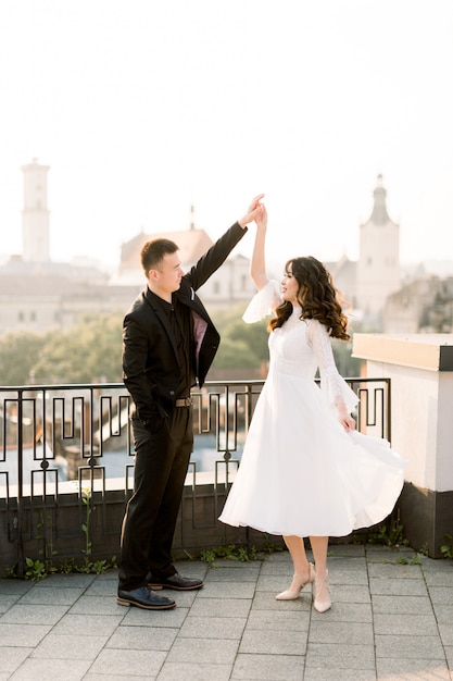 Joven hermosa novia asiática y el novio en el día de la boda caminando y bailando en la azotea de la ciudad vieja.