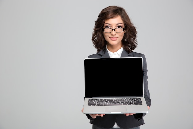 Joven hermosa oficinista con gafas está sosteniendo una computadora portátil frente a sí misma