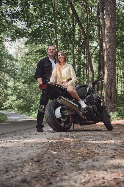 Una joven y hermosa pareja abrazándose sentada en una motocicleta viajan juntos por un camino forestal