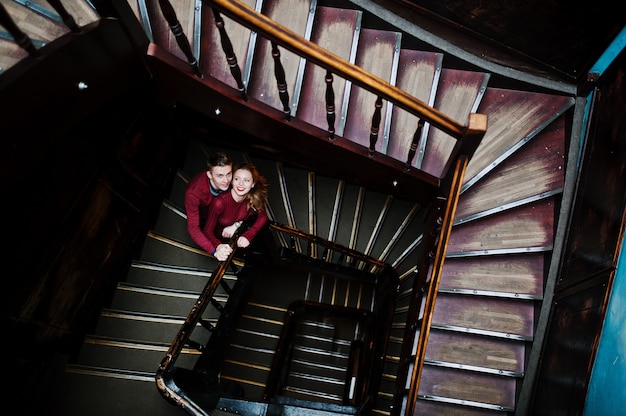 Joven hermosa pareja elegante en un vestido rojo en grandes escaleras vintage de madera