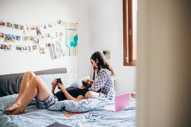 Joven hermosa pareja feliz en el amor acostado en la cama abrazando con tableta