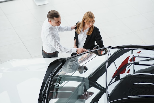 Joven hermosa pareja feliz comprando un coche. Marido comprando un coche para su esposa en un salón. Concepto de compra de coches.