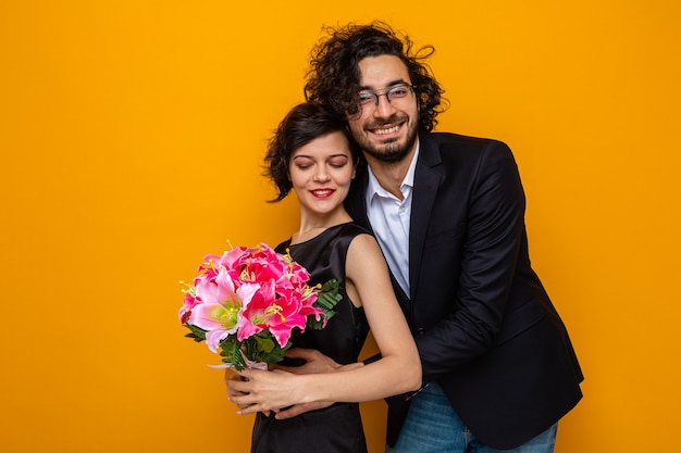 Joven hermosa pareja feliz hombre y mujer con ramo de flores sonriendo alegremente abrazando feliz en el amor celebrando San Valentín