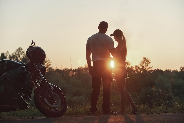 Joven hermosa pareja de motociclistas abrazándose al atardecer viajando juntos en una motocicleta