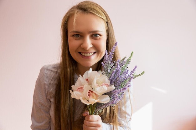 Una joven hermosa con el pelo largo y suelto rubio mantiene las flores de primavera en las manos