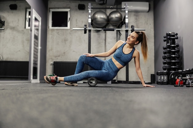 Una joven hermosa en ropa deportiva masajea los músculos laterales de las piernas con un rodillo deportivo masajes