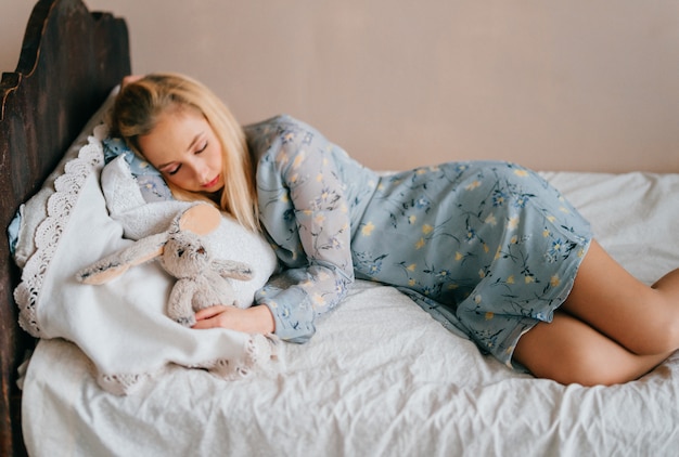 Joven hermosa rubia adolescente durmiendo en la cama de madera vintage con juguete.