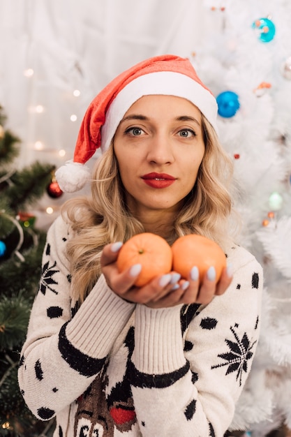 Joven hermosa rubia con sombrero de santa claus con mandarinas en las manos