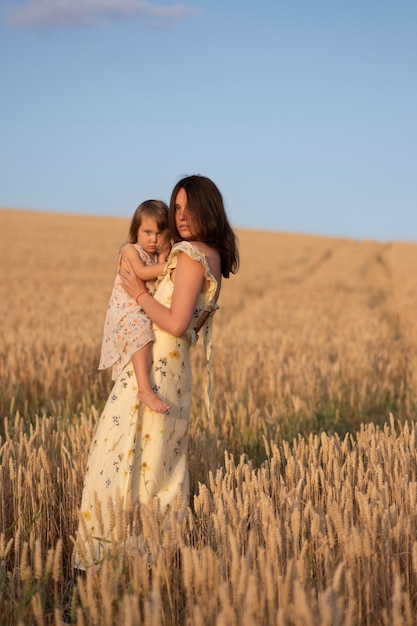 Una joven hermosa sosteniendo a su hija pequeña en un campo al atardecer Una mujer con un niño en un hermoso vestido amarillo posa al anochecer en un campo