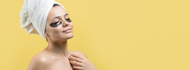 Una joven hermosa con una toalla blanca en la cabeza usa parches de gel de colágeno debajo de los ojos Máscara debajo de la cara de tratamiento de los ojos