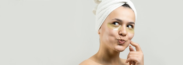 Una joven hermosa con una toalla blanca en la cabeza usa parches de gel de colágeno debajo de los ojos Máscara debajo de la cara de tratamiento de los ojos