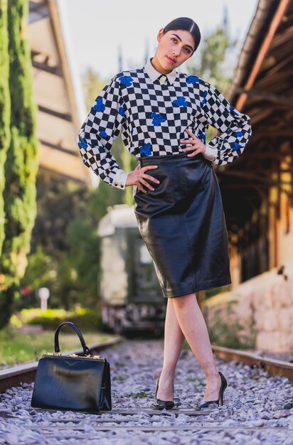 Joven y hermosa turista de estilo retro en la antigua estación de tren, vestida con chaqueta amarilla y negra.