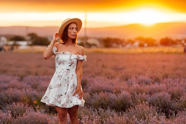 Una joven hermosa con un vestido y un sombrero delicados camina por un hermoso campo de lavanda y disfruta de la fragancia de las flores Descanso y hermosa naturaleza Floración de lavanda y recolección de flores