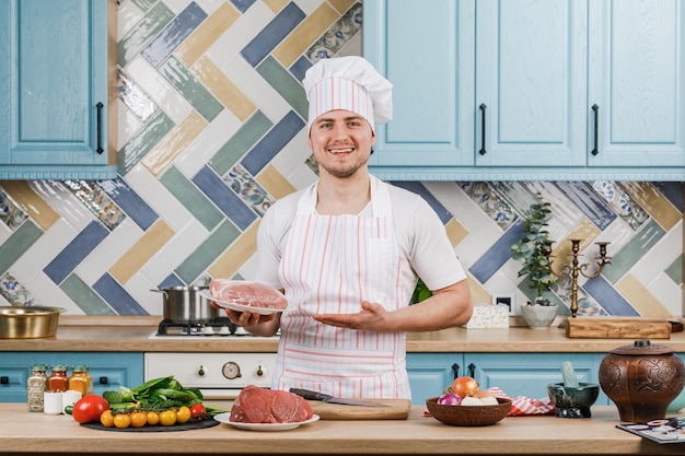 Joven y hermoso chef masculino presenta comida en la cocina