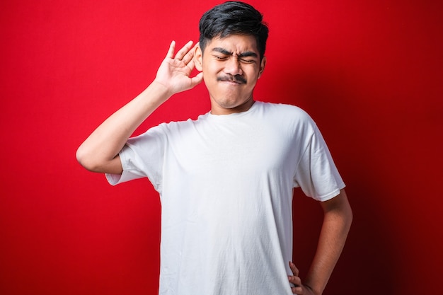 Joven hermoso muchacho asiático con camiseta blanca de pie sobre un fondo rojo que se extiende hacia atrás, cansado y relajado, con sueño y bostezos por la mañana temprano