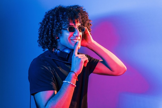 Un joven hermoso con el pelo rizado está en el interior del estudio con luces de neón