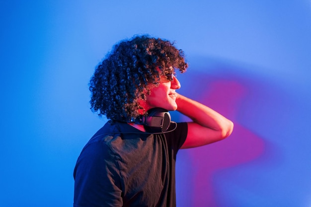 Un joven hermoso con el pelo rizado está en el interior del estudio con luces de neón