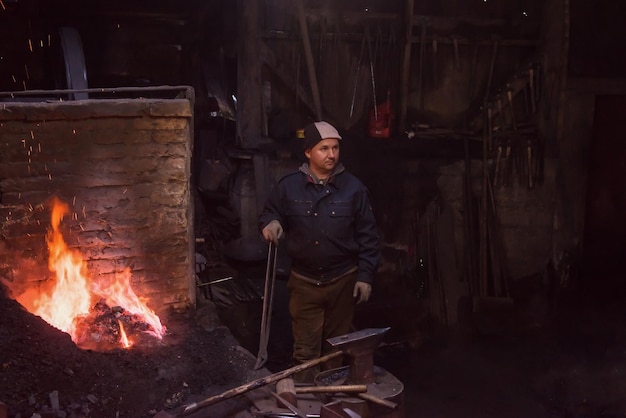 joven herrero tradicional trabajando con fuego abierto El herrero haciendo llamas en la herrería con chispas de fuegos artificiales forjando hierro caliente en el taller