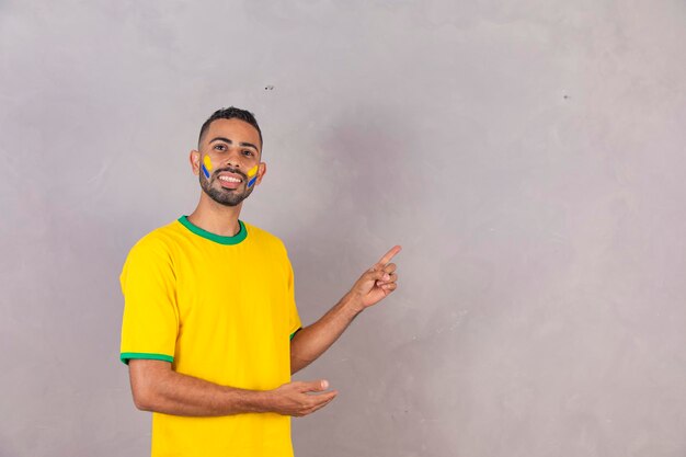 Joven hincha brasileño negro apuntando hacia un lado en espacio libre para texto Foto publicitaria para la copa del mundo