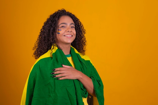 Joven hincha de fútbol brasileña negra con la bandera de brasil cantando el himno nacional