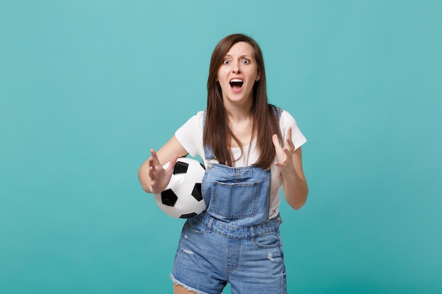 Una joven hincha de fútbol conmocionada apoya al equipo favorito con un balón de fútbol esparciendo las manos aisladas en un fondo azul turquesa de la pared. Emociones de la gente, concepto de ocio familiar deportivo. Simulacros de espacio de copia.