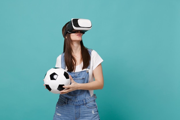 Una joven hincha de fútbol sorprendida mirando con auriculares sosteniendo una pelota de fútbol jugando aislada en un fondo azul turquesa de la pared. Emociones de la gente, concepto de estilo de vida de ocio familiar deportivo. Simulacros de espacio de copia.