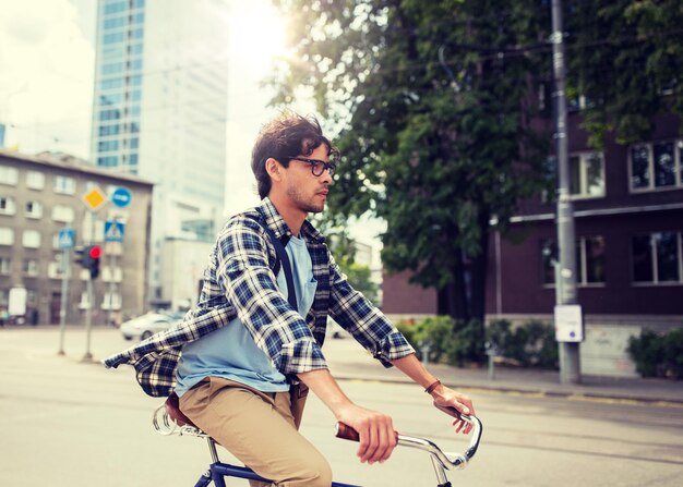 Foto joven hipster con una bolsa montando una bicicleta de engranajes fijos