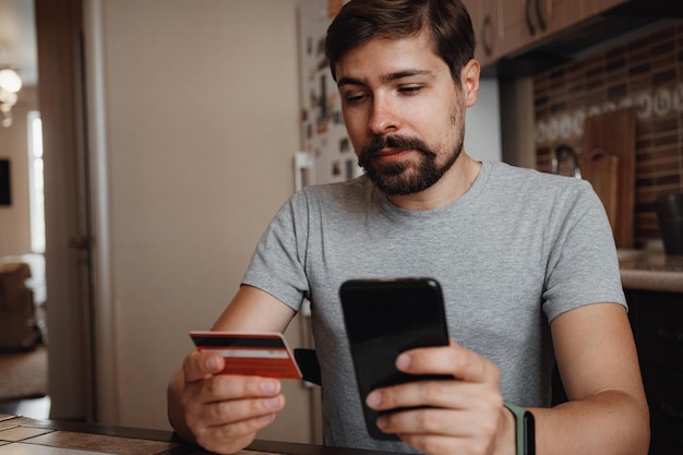 Joven hipster comprando en línea con tarjeta de crédito usando un teléfono inteligente en casa