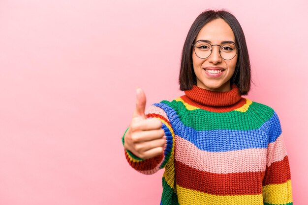 Joven hispana aislada de fondo rosa sonriendo y levantando el pulgar