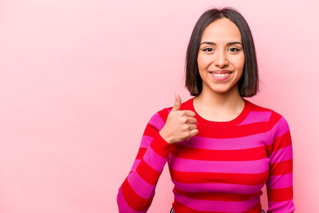 Joven hispana aislada de fondo rosa sonriendo y levantando el pulgar